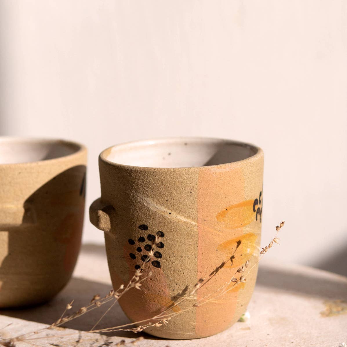 Sleek tumbler featuring a ledge halfway round. Perfect for small drinks and small hands. Raw stoneware finished with handpainted embellishments & white glazed interior. Handmade in Denver, CO.