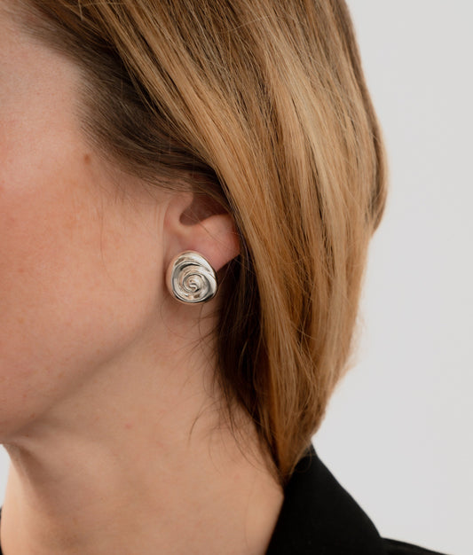 Silver spiral earring worn by a person with a neutral background. Amanda Hunt Compass Earrings