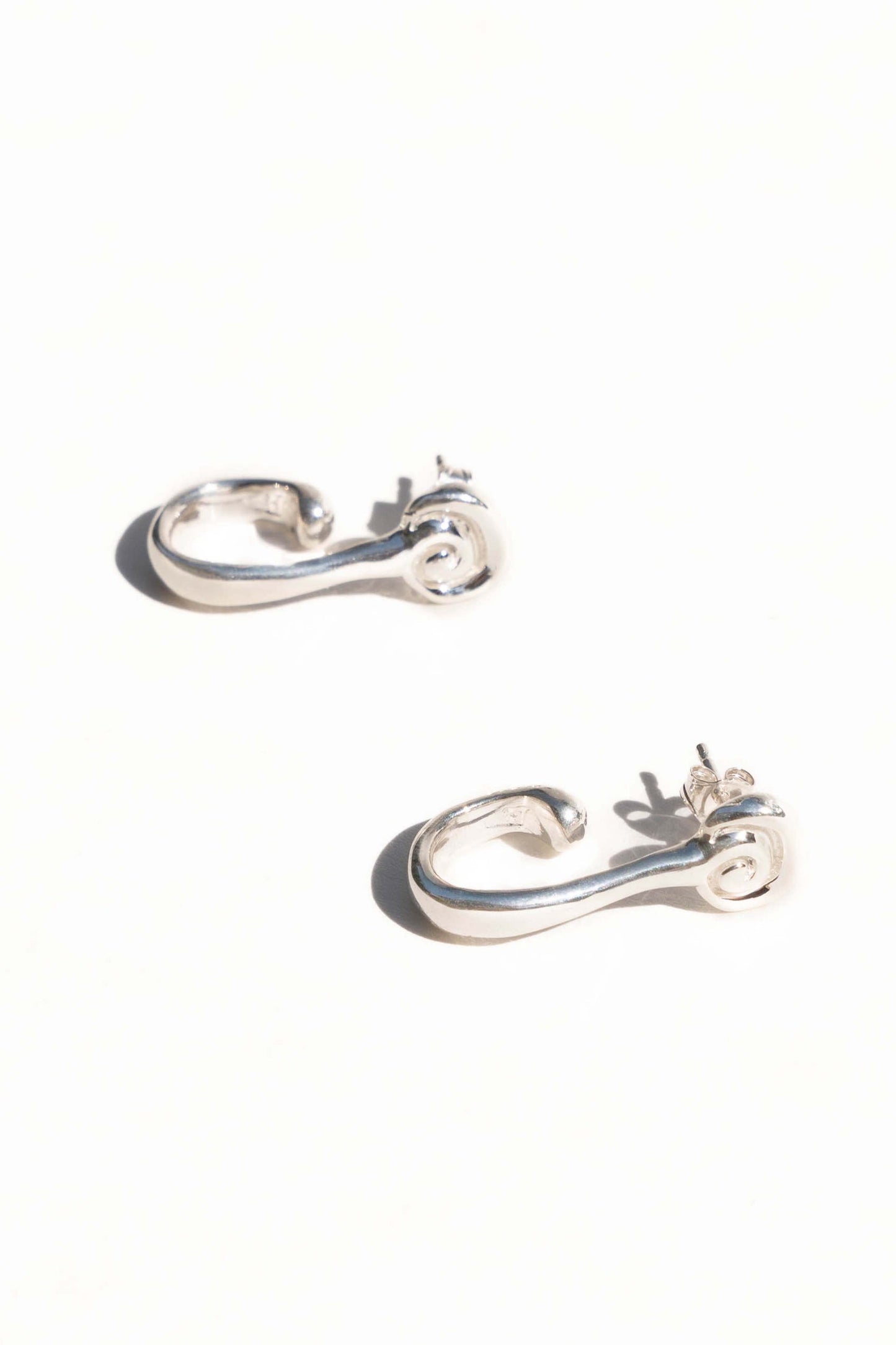 Pair of silver hoop earrings on a white background. Moneh Brisel Espira Earrings