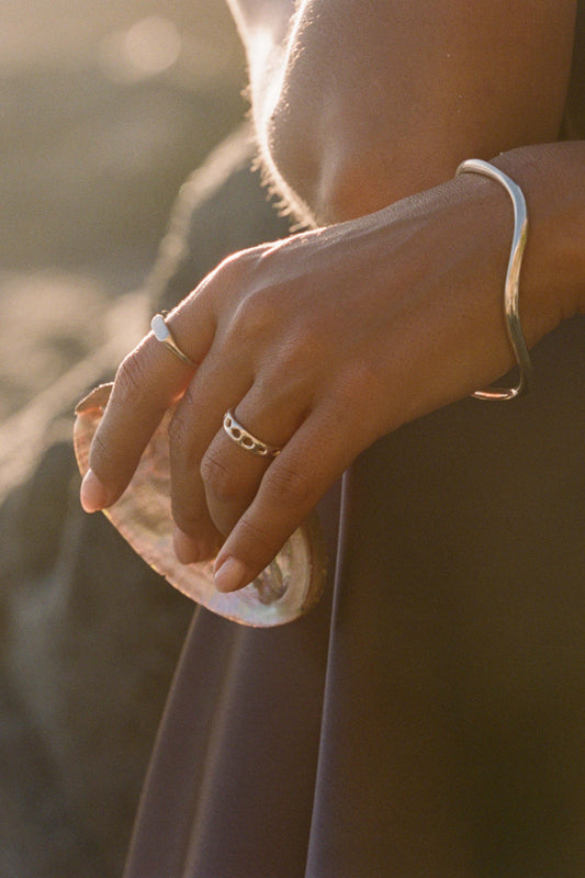 Close-up of a person's hand holding a shell with sunlight casting a warm glow on her handmade sterling silver Moneh Brisel jewelry.
