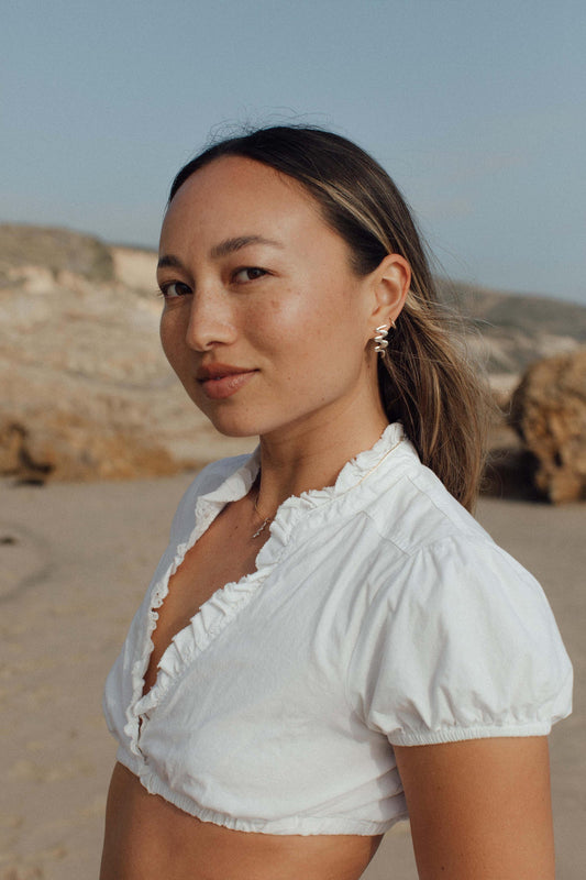 Woman wearing a white blouse on a beach with mountains in the background. Moneh Brisel Kombu Earrings