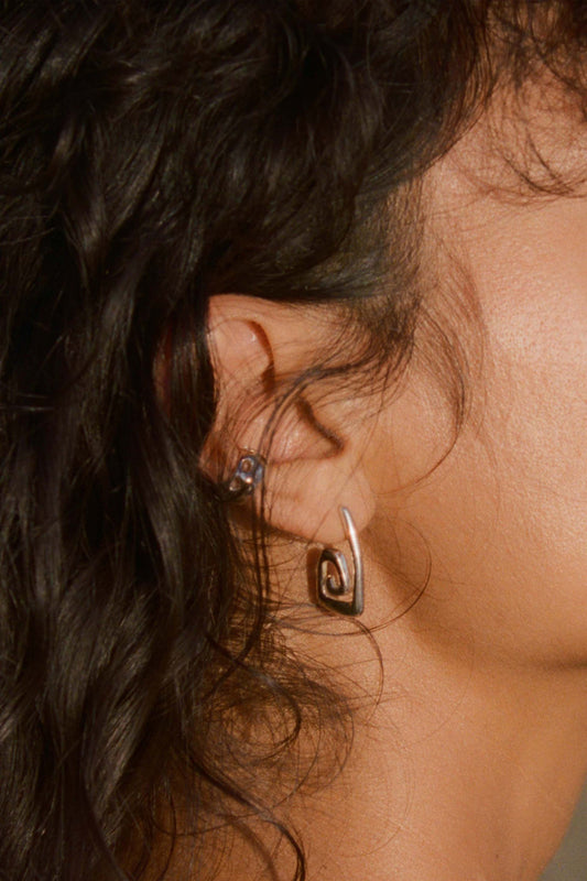 Close-up of an ear with earrings and hair. Moneh Brisel Nautilo Earrings