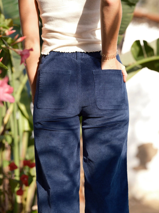 Person wearing blue corduroy pants with a blurred natural background. Mollusk Surf Shop Mid Rise Corduroy Painter Pants