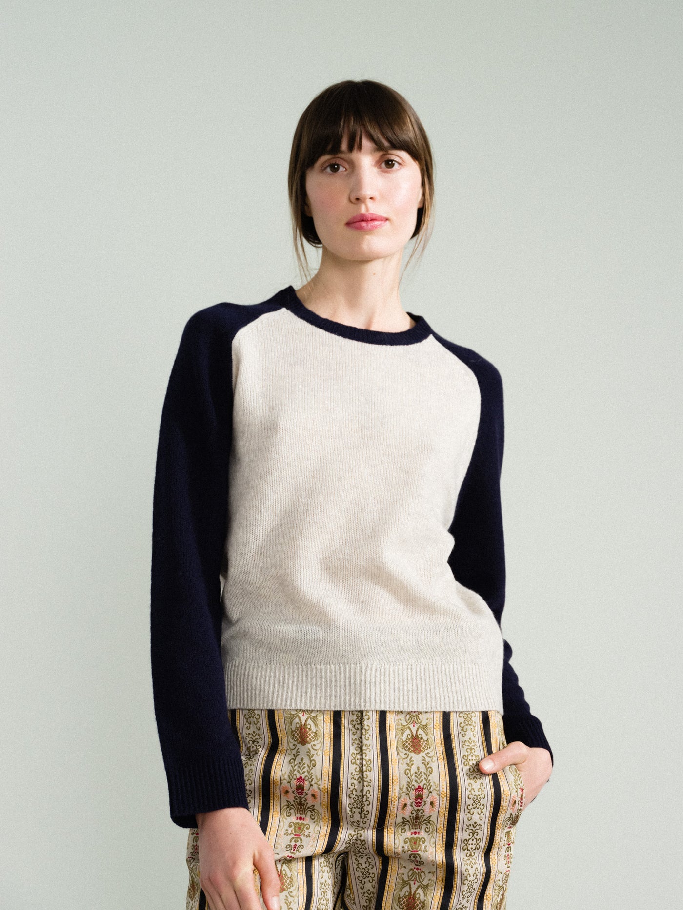 Person wearing a white and navy sweater with patterned pants on a plain background
