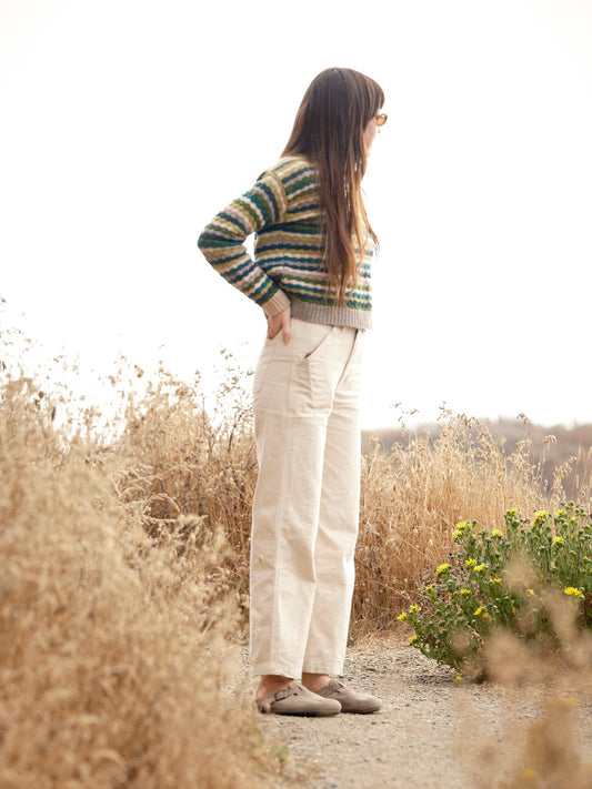 Woman in a striped sweater and white pants standing in a natural setting with dry grass and wildflowers. Mollusk Surf Shop Kilim Sweater