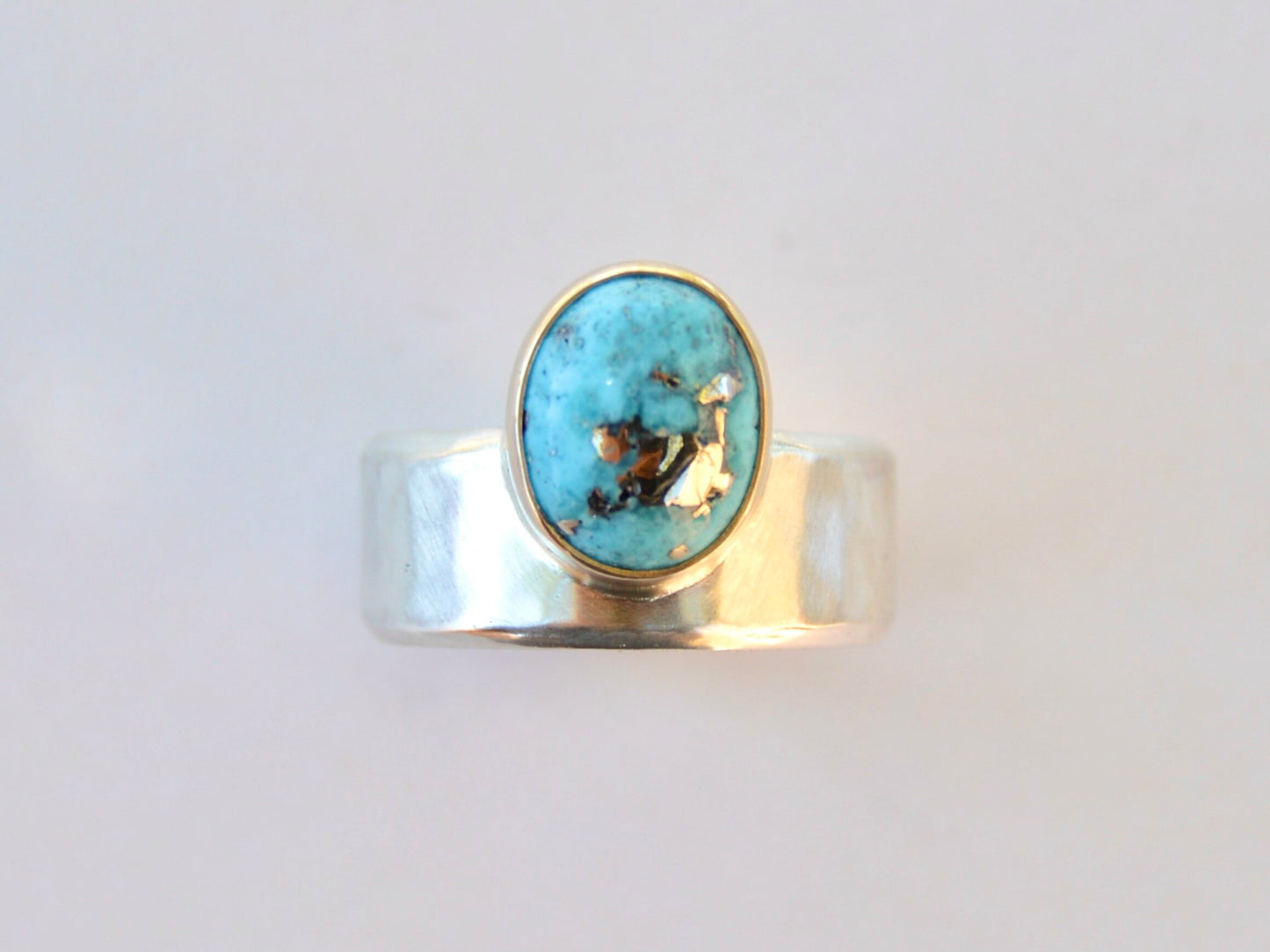 Made by hand in Northern New Mexico using recycled metals and responsibly sourced stones. This ring features a large cabochon Persian Turquoise stone set in a 14k yellow Gold bezel on a wide Sterling Silver band with matte finish. Mesa Ring by Halcyon Jewelry.
