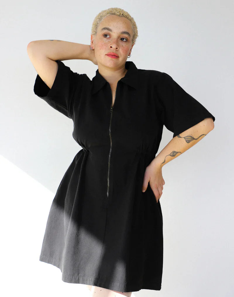 The Noble utility dress in black worn by a woman posing with her arm over her head