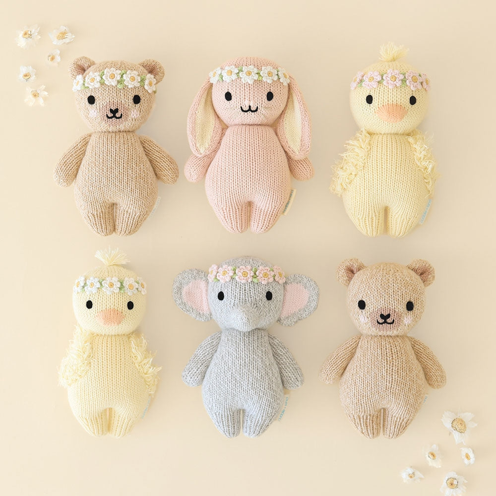 Sustainable stocking stuffers for kids by Cuddle and Kind - hand-knit cotton dolls that give meals to kids in need. A selection of fair trade stuffed animals against a tan background.