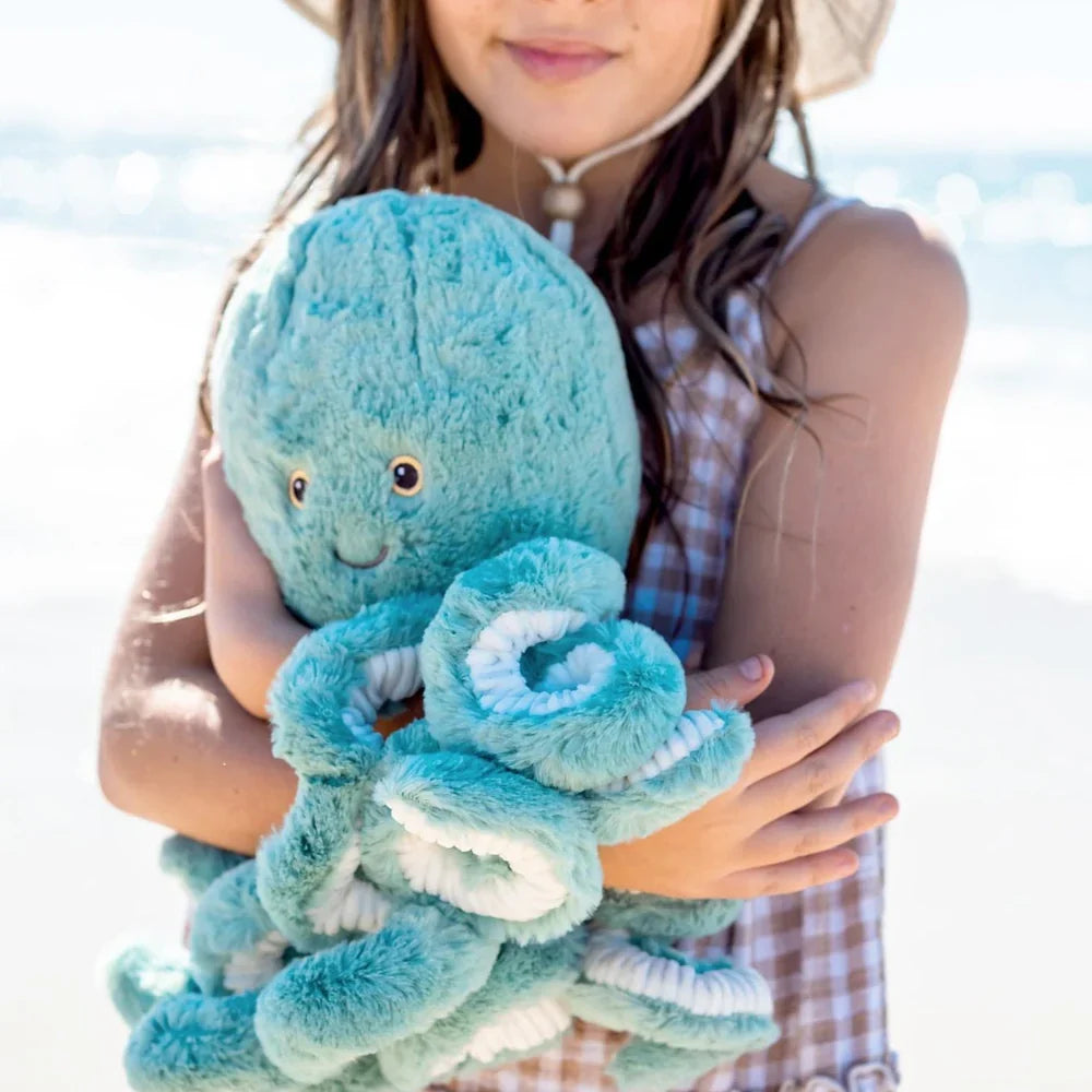 Girl holding a soft stuffed animal octopus in a blue color at the beach