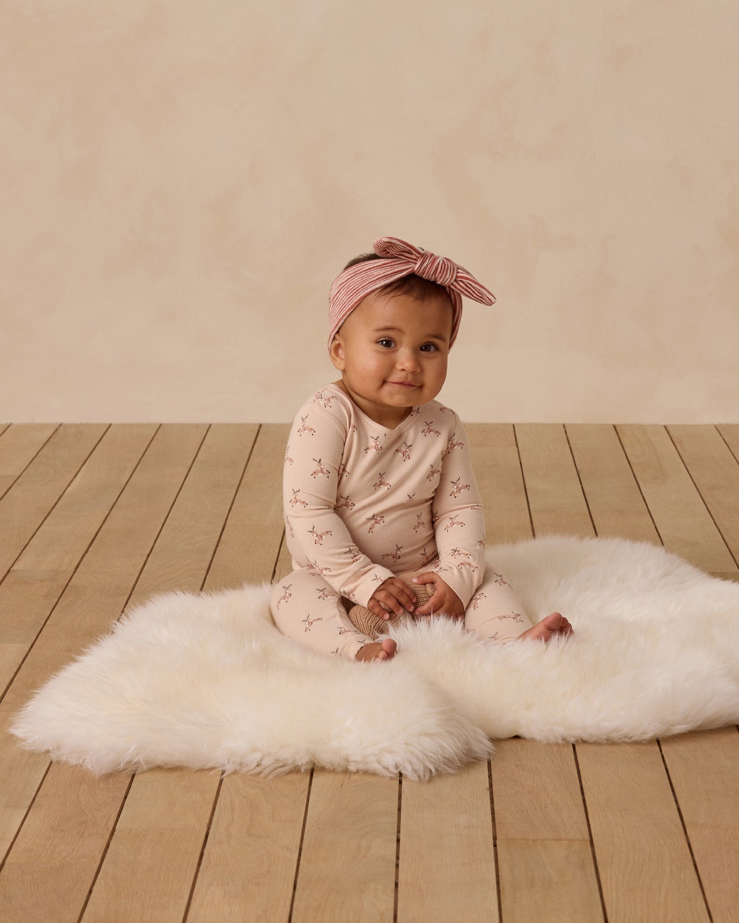 A baby sits on an organic shag rug wearing bamboo holiday pajamas by Quincy Mae