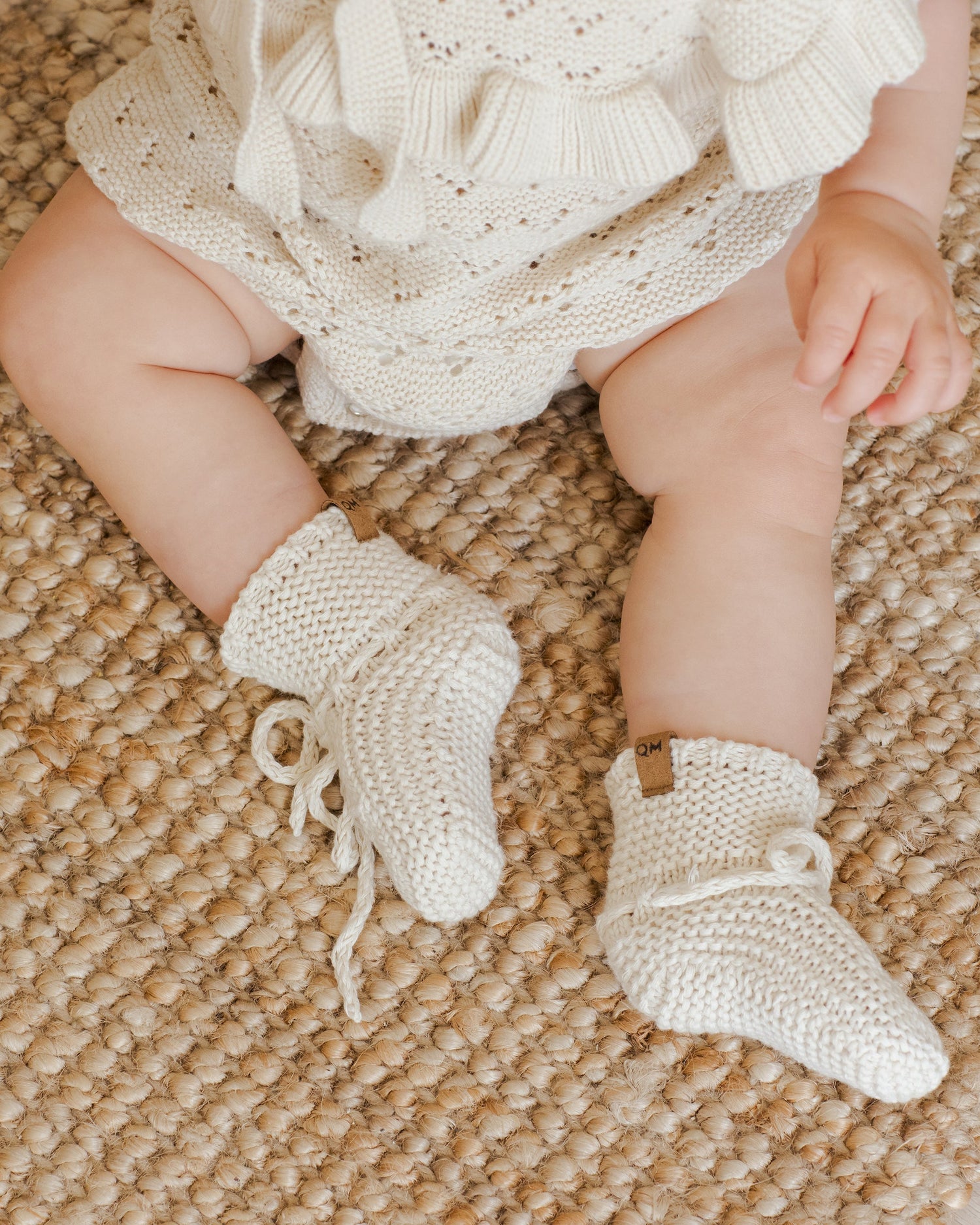 An infant sits up wearing hand knit baby booties, the perfect newborn baby gift