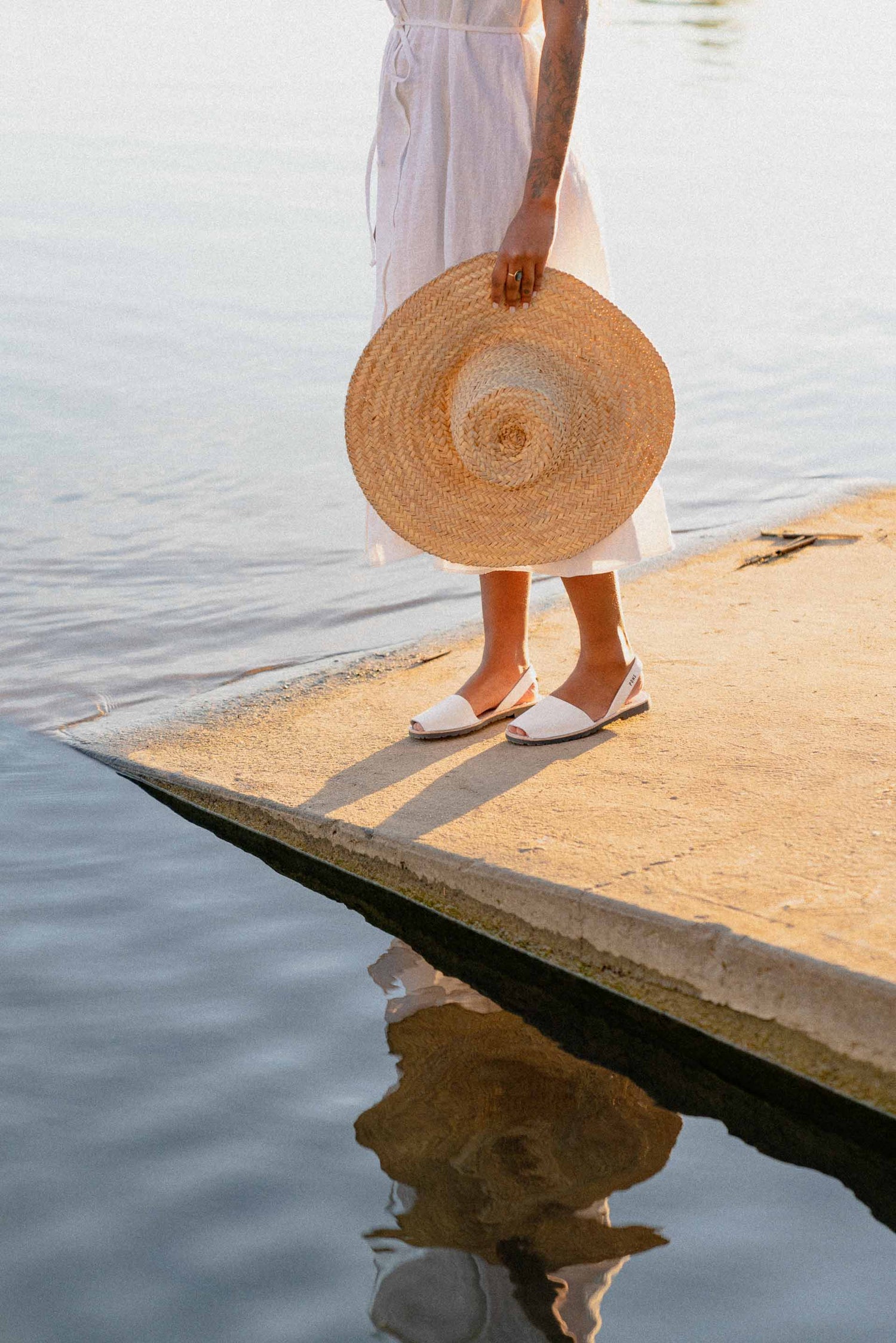 Pons leather sandals are ethically made in Spain, pictured here in white on a woman standing near water