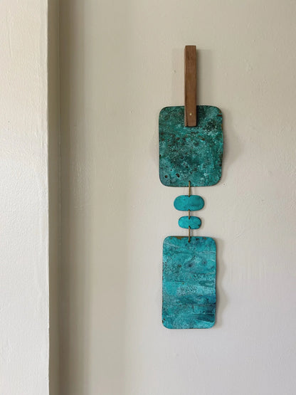Turquoise wall art with wooden elements on a white wall. Wall hanging made of patinated brass pieces and hammered brass rod connection and a wooden shape. Handmade in NorCal.
