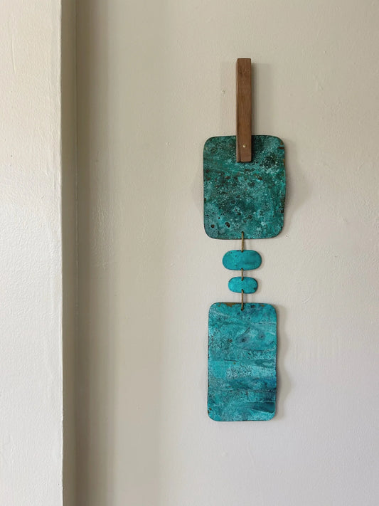 Turquoise wall art with wooden elements on a white wall. Wall hanging made of patinated brass pieces and hammered brass rod connection and a wooden shape. Handmade in NorCal.