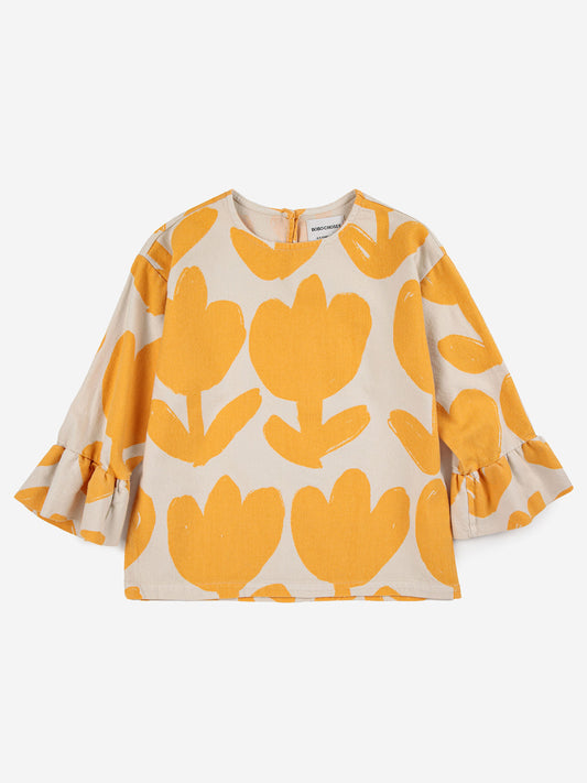 Bobo Choses Big Flower Ruffle Blouse. 100% cotton off white blouse with yellow flowers. Designed with long sleeves, back button fastening, embroidery, round neck and ruffled detailing. It has a evasé fit.  Sustainably and ethically made in Spain.