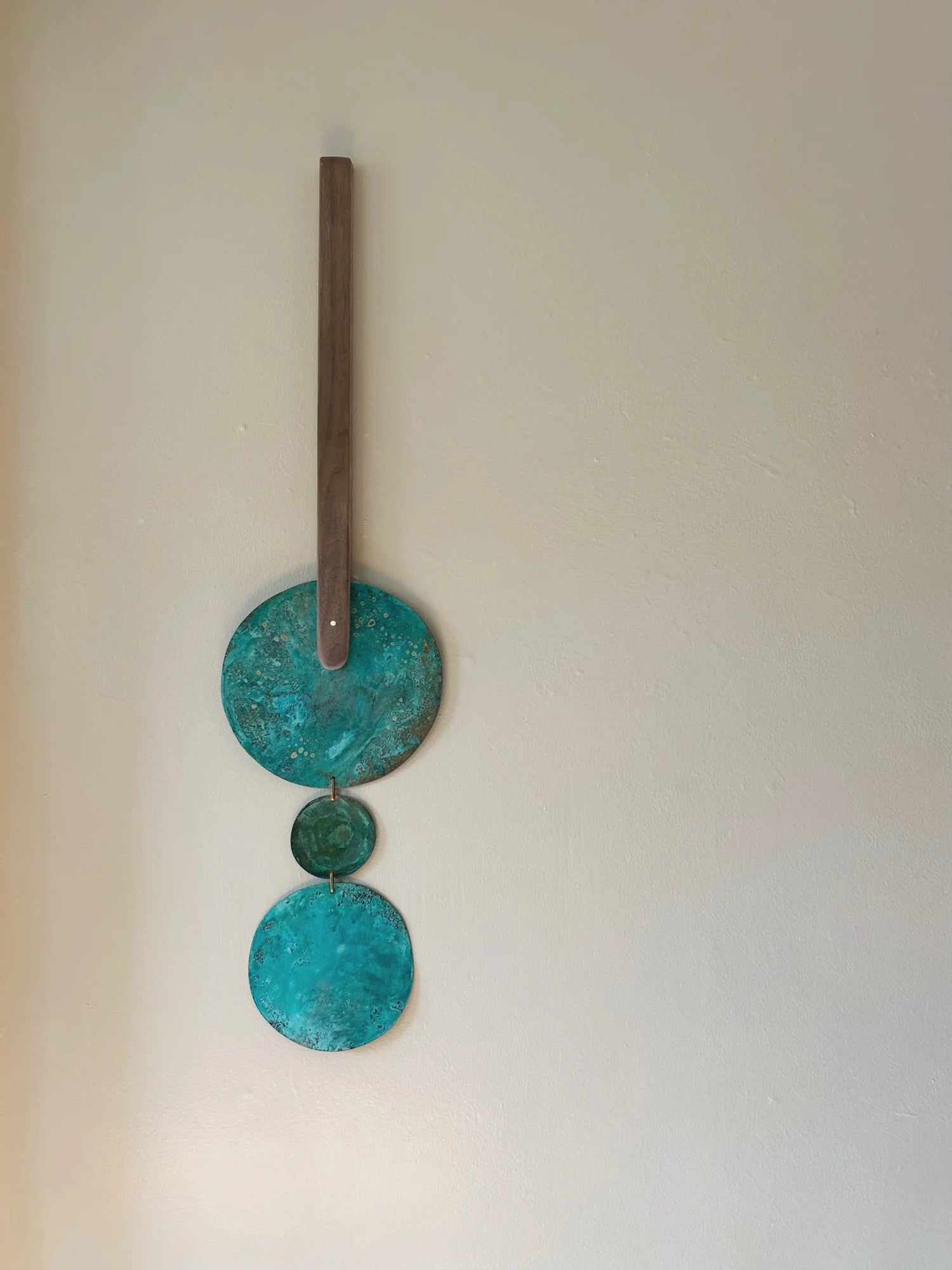 Decorative wall hanging with three turquoise circular discs and a wooden stick on a plain background. Wall hanging made of patinated brass pieces and hammered brass rod connection and a wooden shape. Handmade in NorCal.