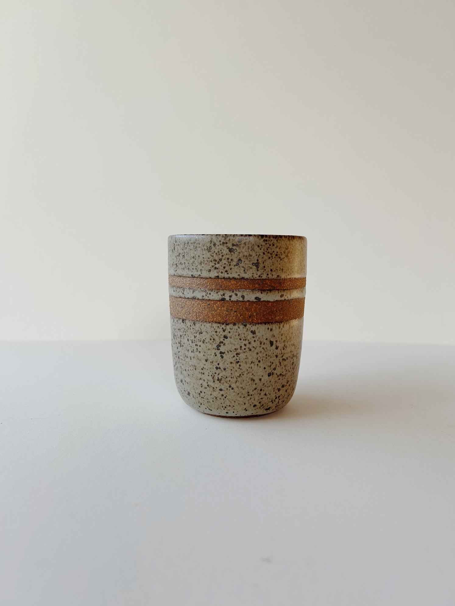 A matte grey and speckled ceramic tumbler cup with raw clay rings for a nice hand grip.  Made-by-hand, by Lisa Fontaine in her home studio in Berkeley. CA.