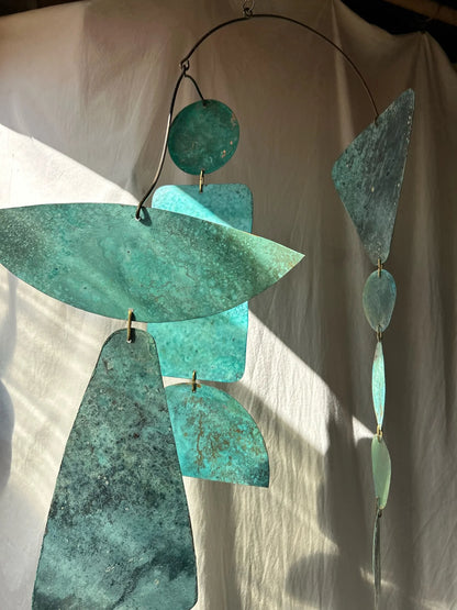 Decorative metal sculpture with teal and green tones on a neutral background. Kinetic piece made of patinated brass pieces and manipulated brass rod. Handmade in NorCal.