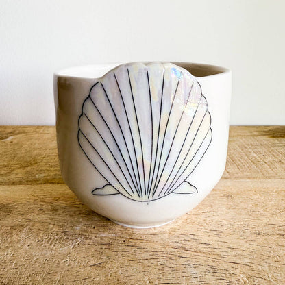 Seashell cups are hand-thrown from fine porcelain, and feature hand drawn inlay and mother of pearl luster for a delicate and iridescent shine.