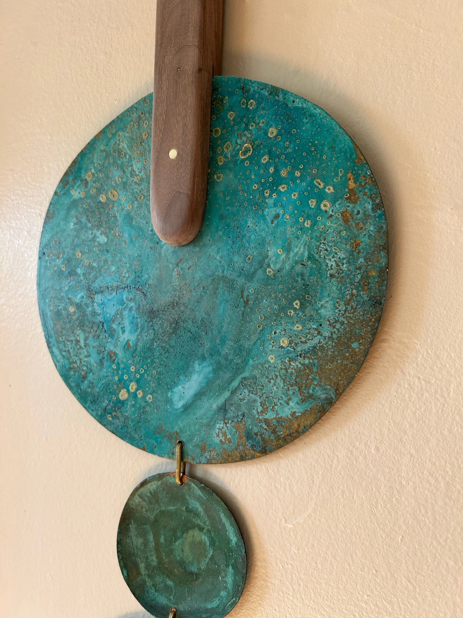 Decorative wall piece with turquoise circular plates and a wooden handle on a beige background. Wall hanging made of patinated brass pieces and hammered brass rod connection and a wooden shape. Handmade in NorCal.