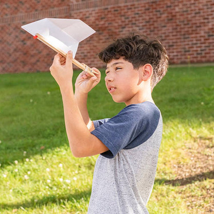 Boy plays with an FSC birch wood paper plane launcher outside on grass with a brick background