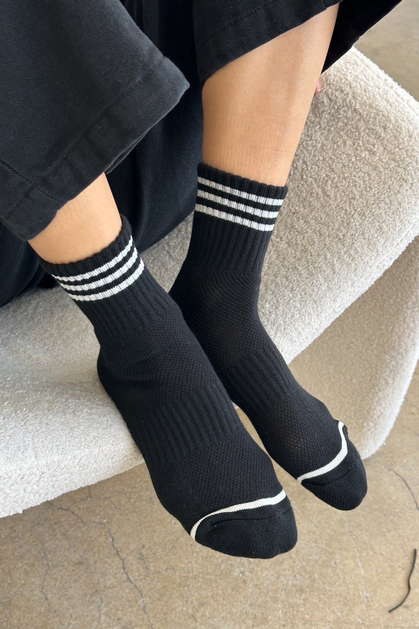 Black socks with white stripes worn by a person sitting on a textured surface.