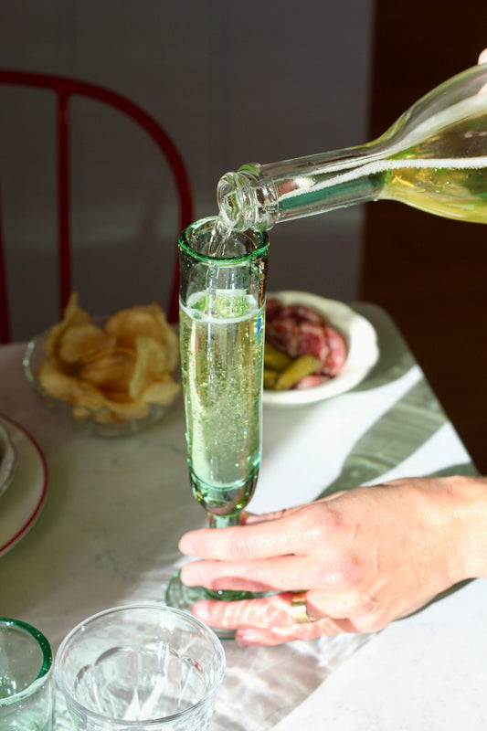 A playful champagne flute with a unique silhouette, designed to keep the party going. Each glass is handmade from recycled glass by artisan partners in Bogotá, Colombia, giving every piece its own subtle character.