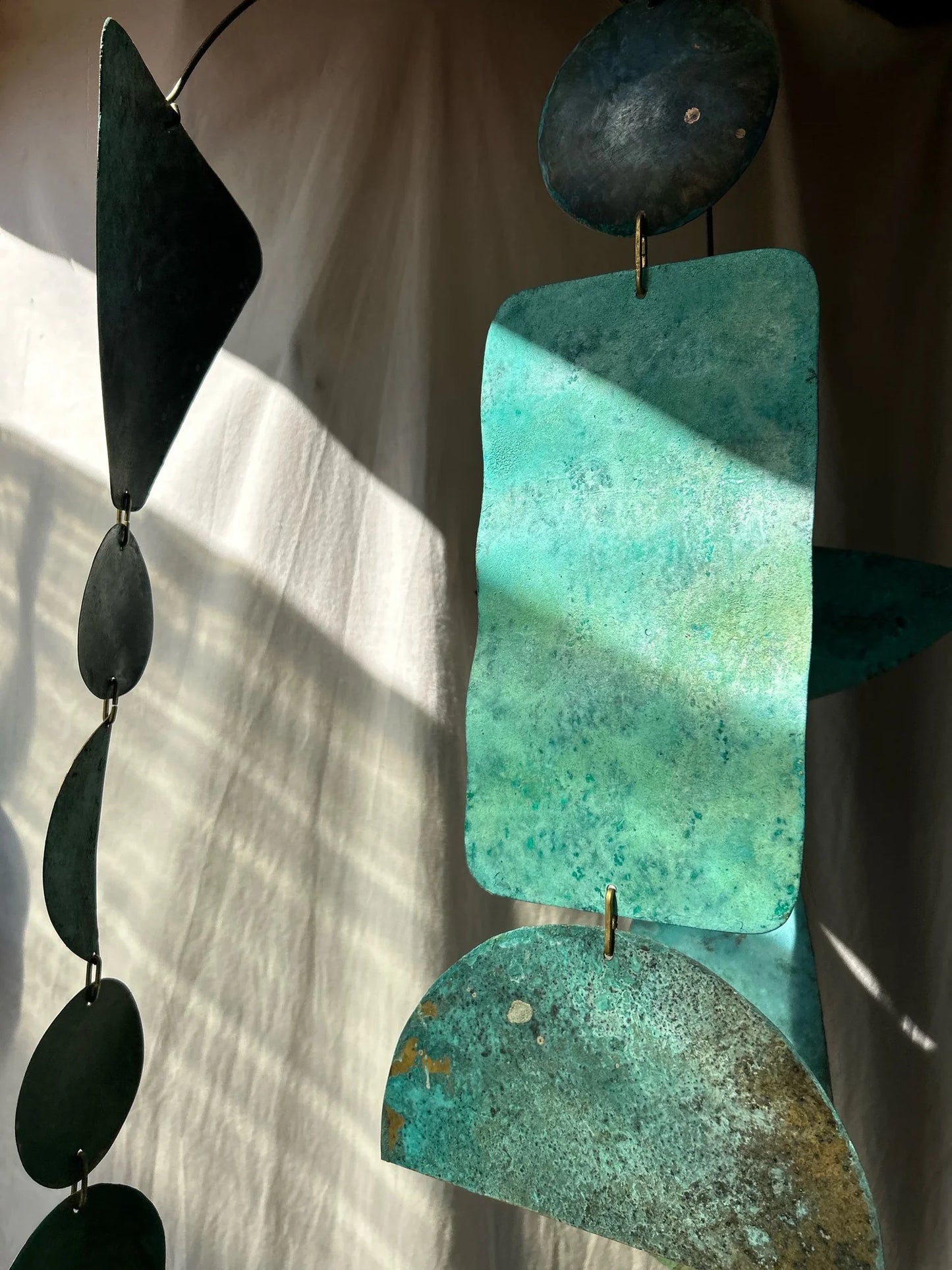 Decorative hanging with green and black geometric shapes on a neutral background. Kinetic piece made of patinated brass pieces and manipulated brass rod. Handmade in NorCal.