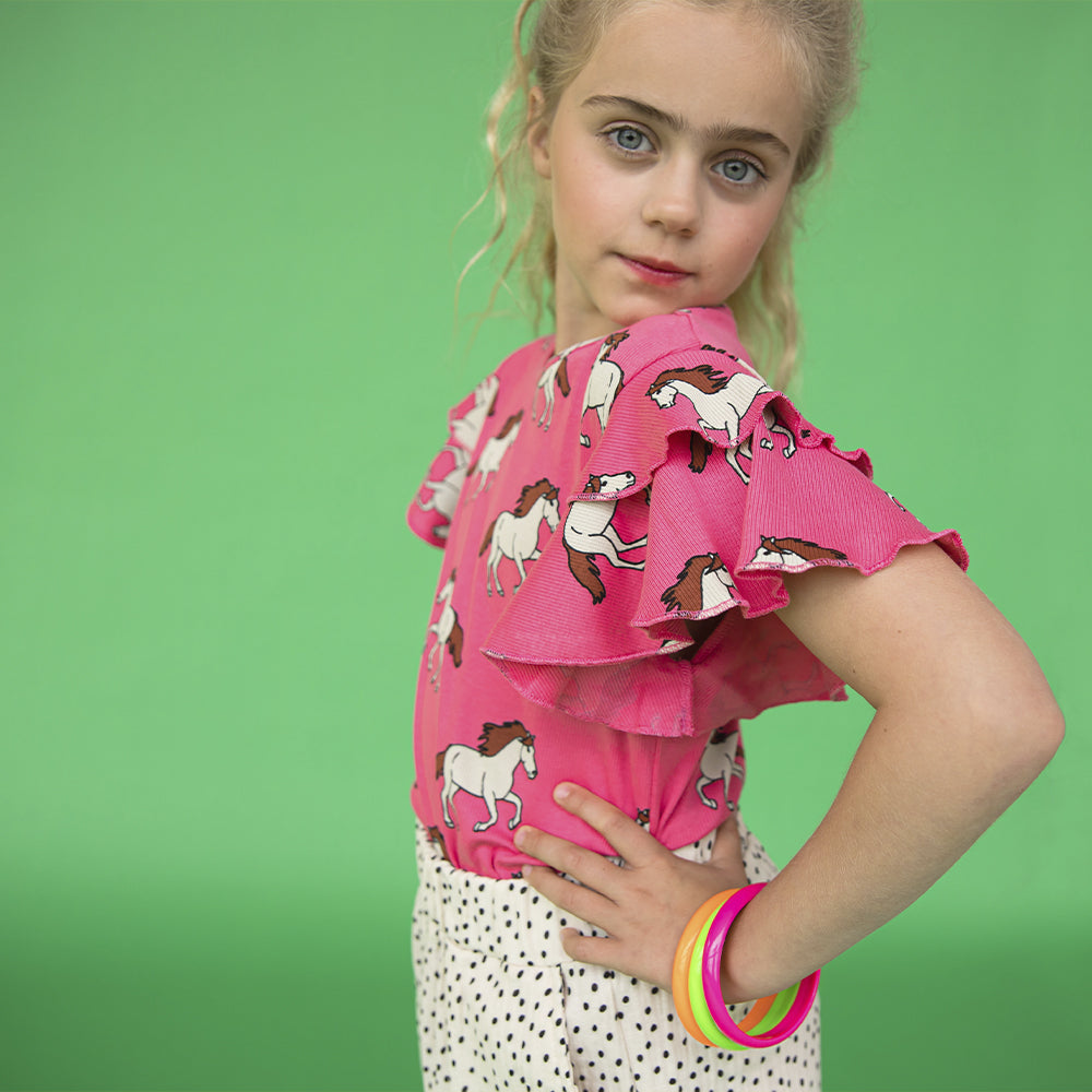 A pink top printed with horses - round neck with ruffle shoulders for fluid movement. Ethically produced, colorful and fun with an eye towards comfort, style and joy. Modern and sustainable kids clothing by CarlijnQ of the Netherlands.