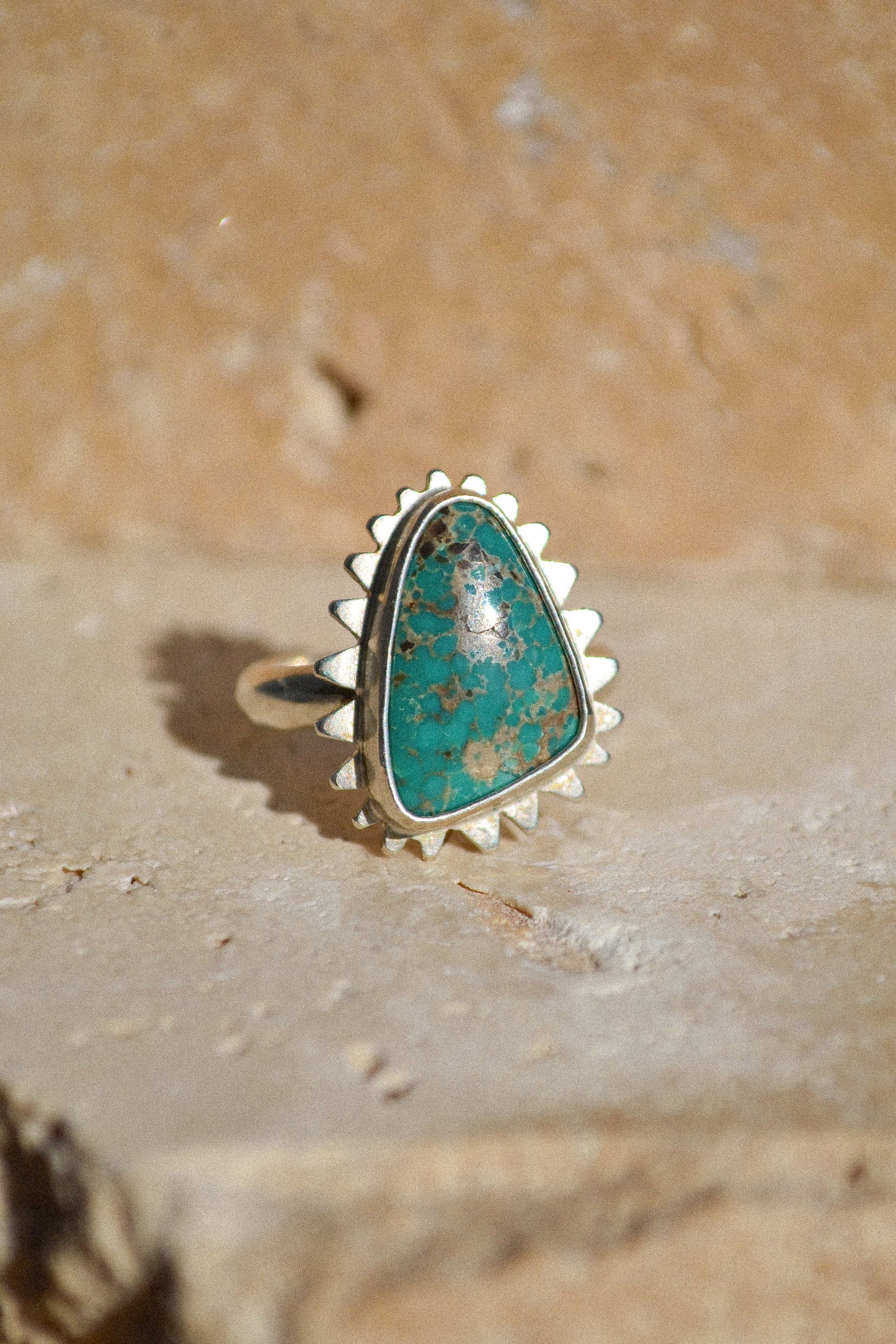 This is a gorgeous triangular turquoise stone deep aqua blue with brown and tan mottling. The stone is set in a thick bezel with hand cut starburst surround. 925 sterling silver