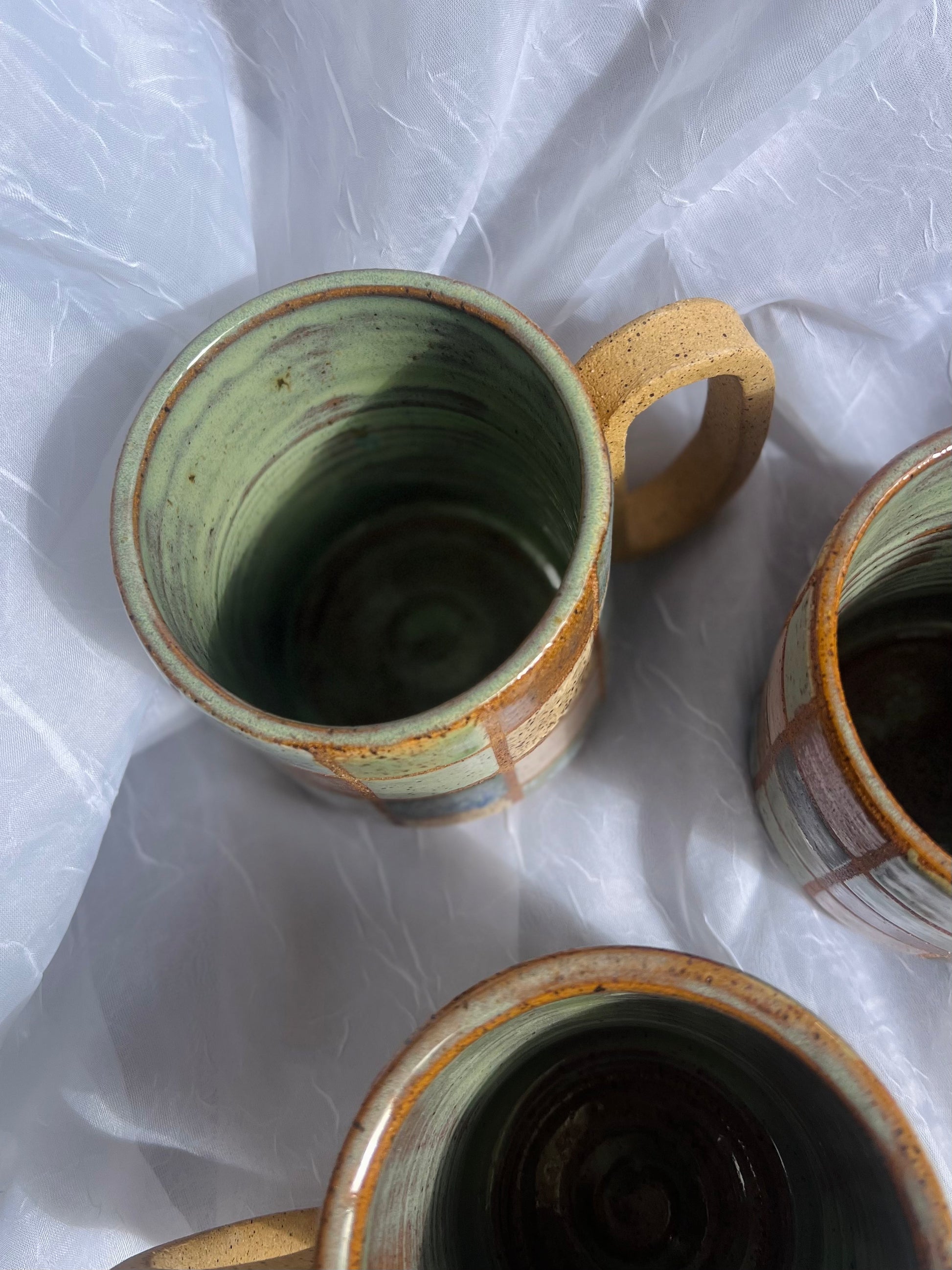 Three ceramic mugs with green and brown glaze on a white fabric background