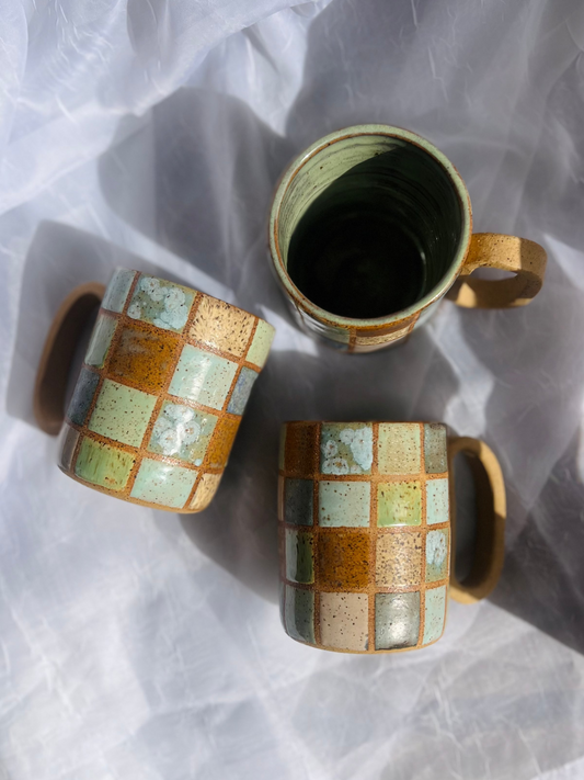 Two ceramic mugs with checkered pattern on a white fabric background