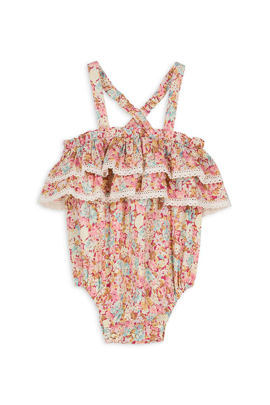Louise Misha Kumal Romper in sweet pink pastel. A floral print romper adorned with lace edged ruffles that features adjustable, elasticized, straps crossed in the back, elasticized legs, and a crotch snap opening. Made with 100% organic cotton including the lining.