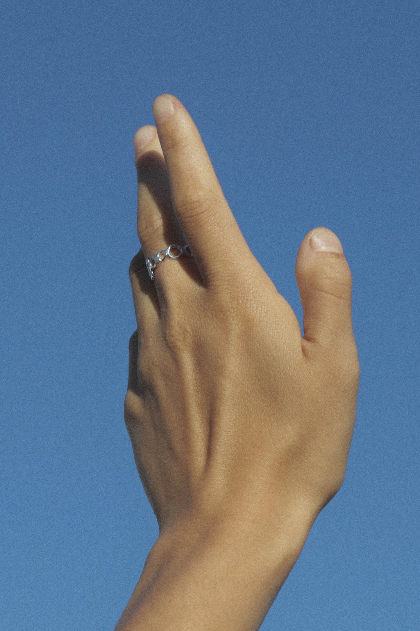 Hand with a ring on a clear blue sky background. Moneh Brisel Current Ring