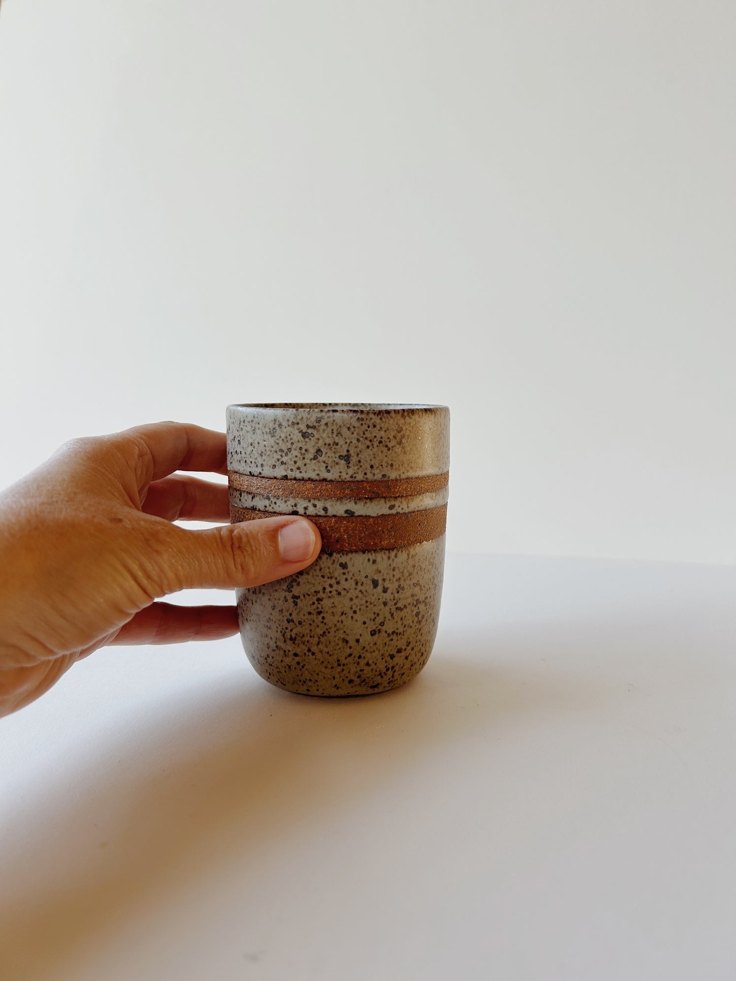 A matte grey and speckled ceramic tumbler cup with raw clay rings for a nice hand grip.  Made-by-hand, by Lisa Fontaine in her home studio in Berkeley. CA.