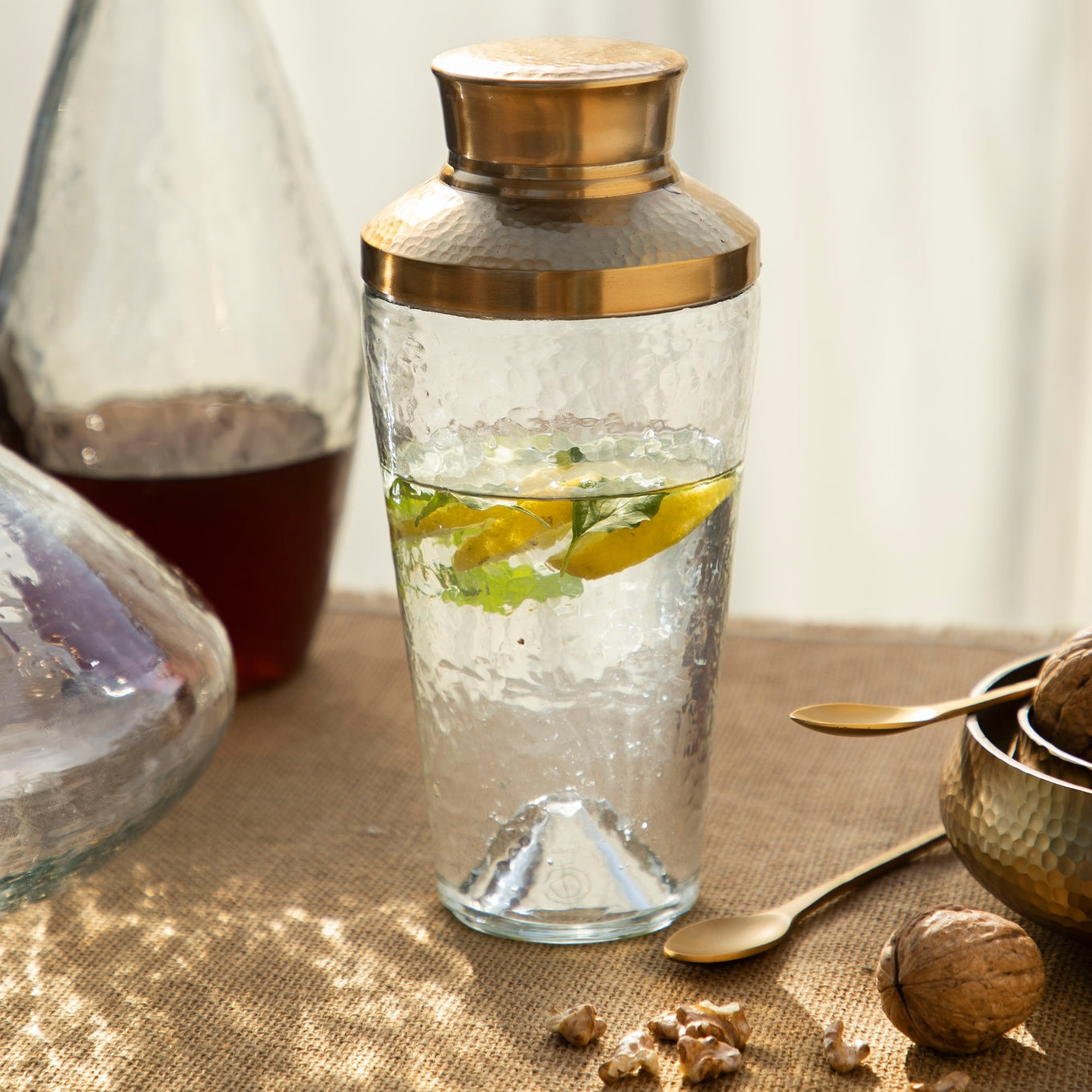 Elevate your mixology game with this stylish pebbled glass cocktail shaker, featuring a hammered, brass-like stainless steel lid crowning a lightly dimpled glass body. 