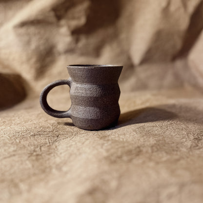 Dark brown ceramic mug on a textured beige surface
