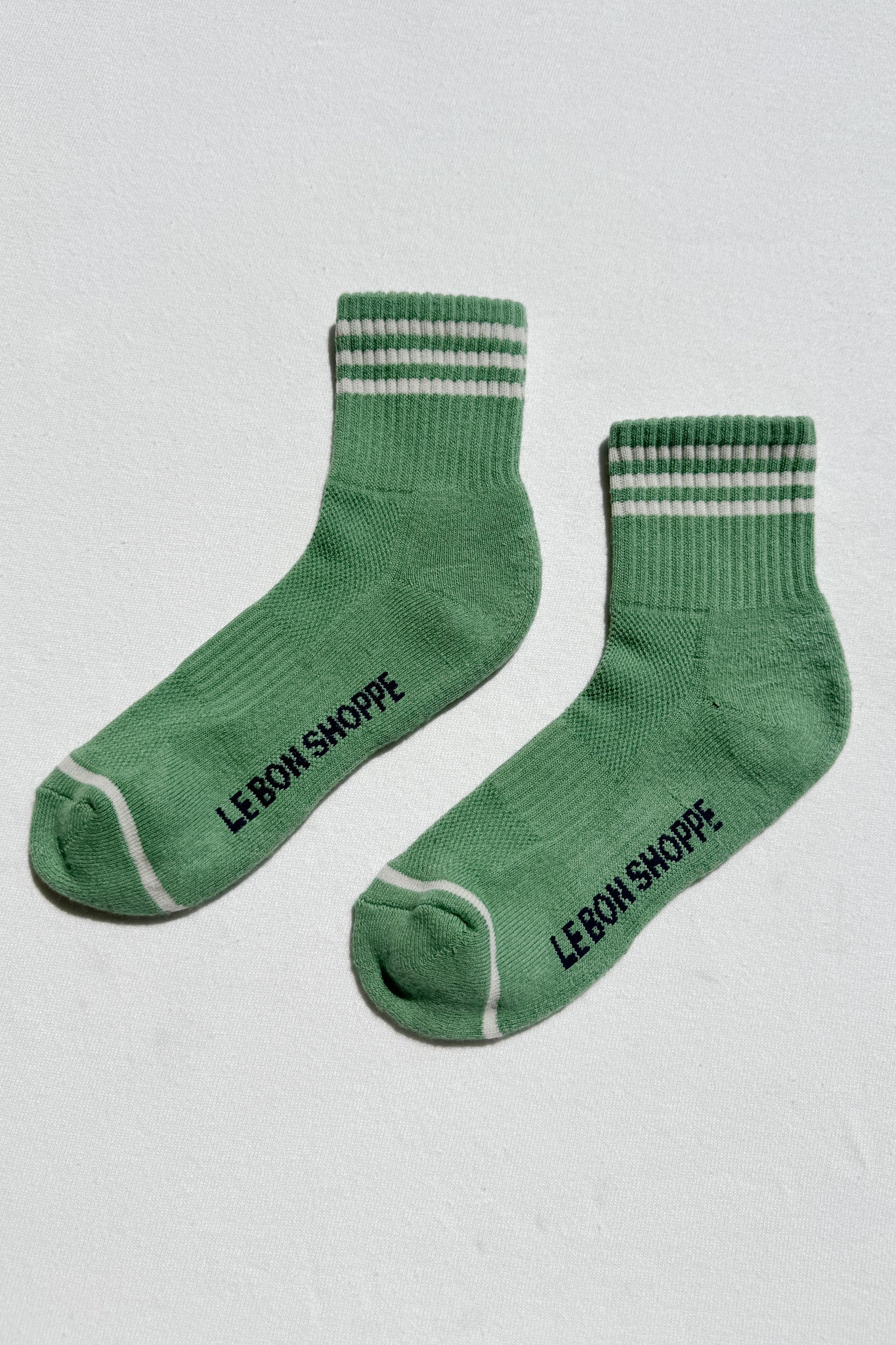 Green socks with striped cuffs and 'Le Bon Shoppe' branding on a light gray background