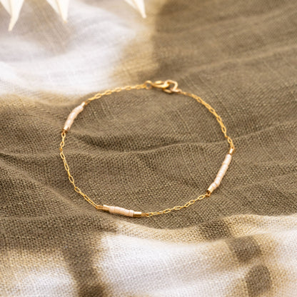 Gold bracelet with small beads on a textured fabric background