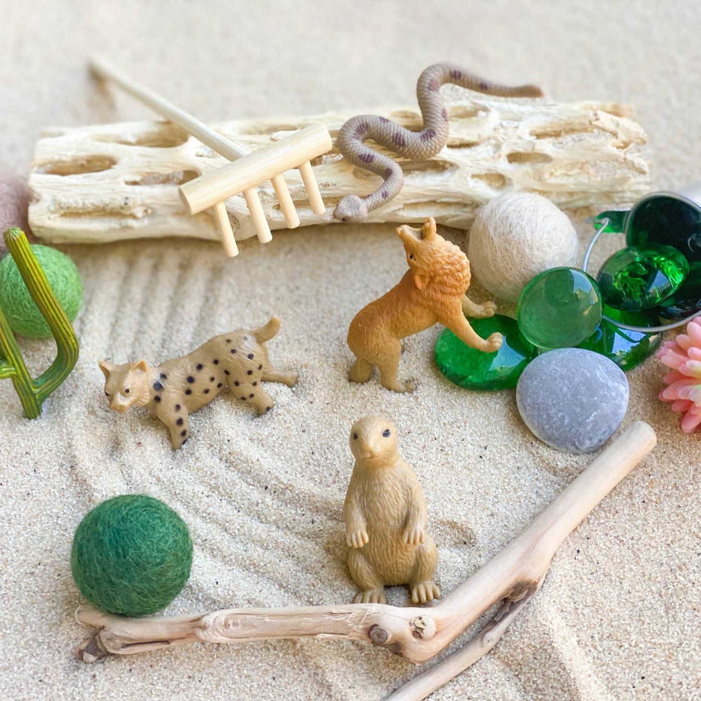 casita curated play sensory kit / Sparkly red play sand is accompanied by a wooden sand rake, authentic cholla and driftwood. Four animals, cactus and felt balls complete the scene.