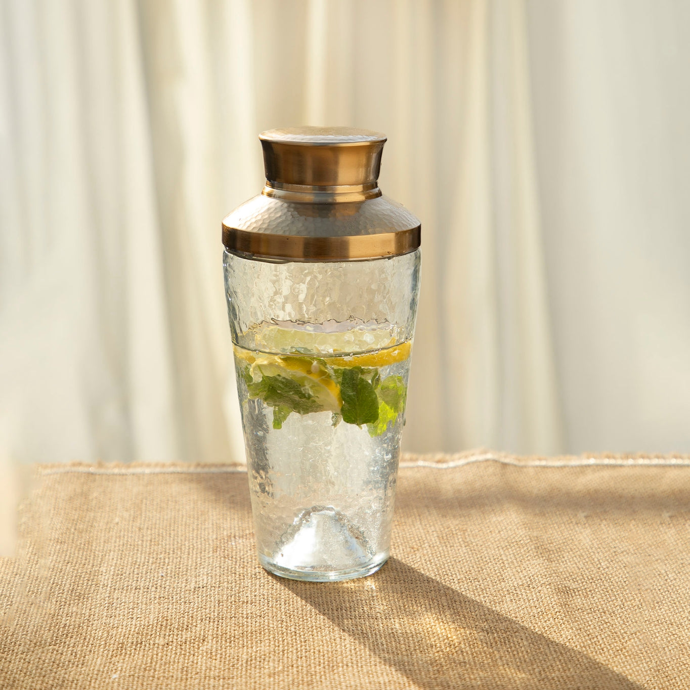 Elevate your mixology game with this stylish pebbled glass cocktail shaker, featuring a hammered, brass-like stainless steel lid crowning a lightly dimpled glass body. 