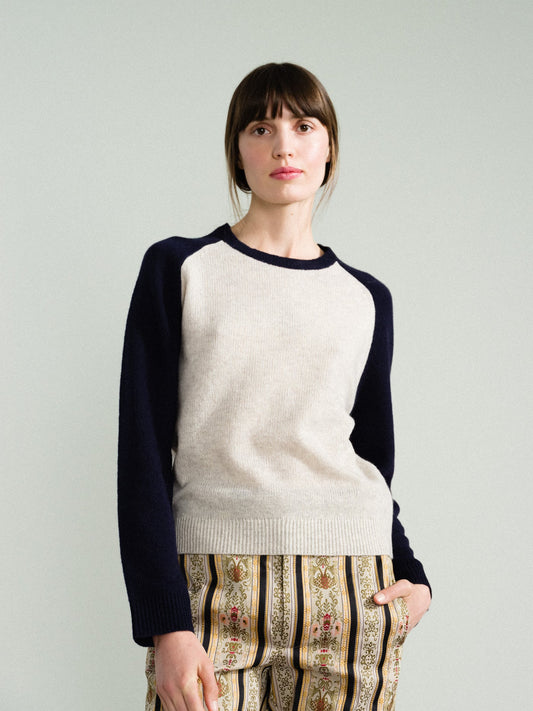 Person wearing a white and navy sweater with patterned pants on a plain background