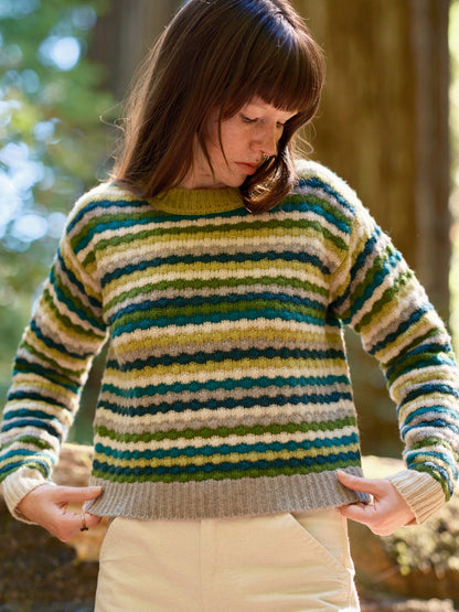 Woman wearing a striped sweater in a forest setting. Mollusk Surf Shop Kilim Sweater
