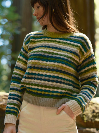Person wearing a striped sweater in a forest setting. Mollusk Surf Shop Kilim Sweater