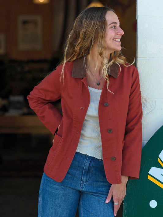 Woman wearing a red jacket and blue jeans standing indoors. Mollusk Surf Shop Lined Painter Jacket 