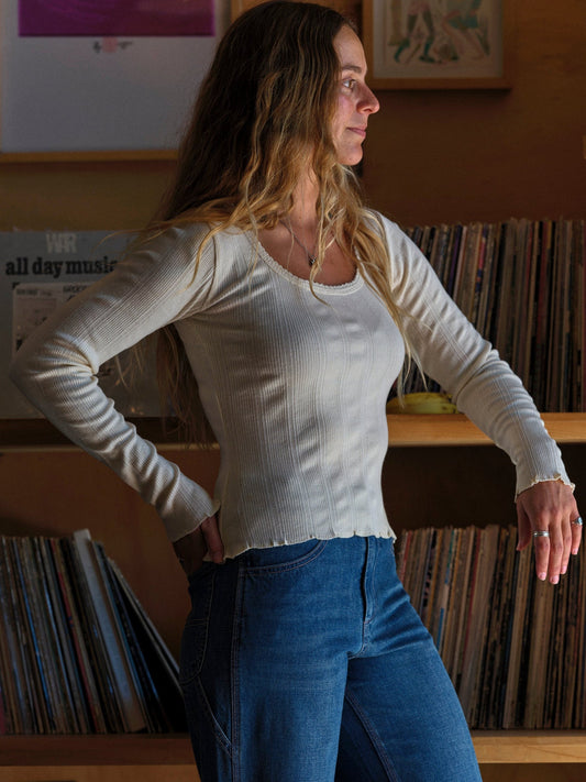 Woman in a white long-sleeve top and blue jeans standing in front of a record collection. Mollusk Surf Shop Pointelle Long Sleeve Tee