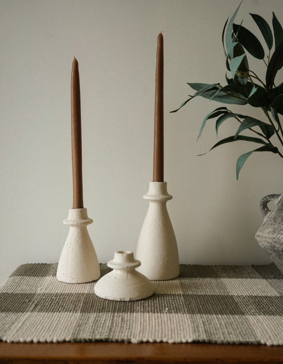 Three ceramic candle holders with brown candles on a checkered tablecloth.