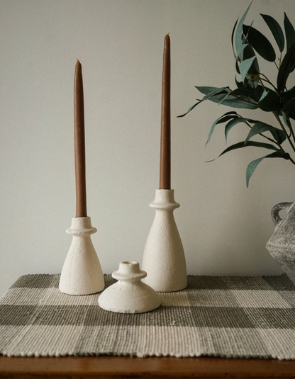 Three ceramic candle holders with brown candles on a checkered tablecloth.