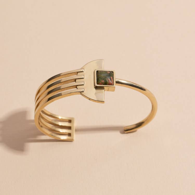 beautifully balanced and uniquely elegant, the deco bracelet is an asymmetrical cuff drawing inspiration from the symmetry of art deco style. handmade, solid brass adjustable cuff with square bar and semi-circle detailing, square set unakite stone on top.