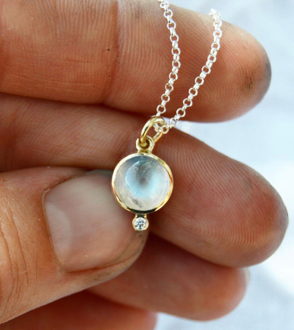 Made by hand in Northern New Mexico using recycled metals and responsibly sourced stones, this timeless, heirloom piece is sure to make a statement.    Polished moonstone sits next to a white diamond, held 14kt yellow gold with an 18" sterling silver rolo chain.